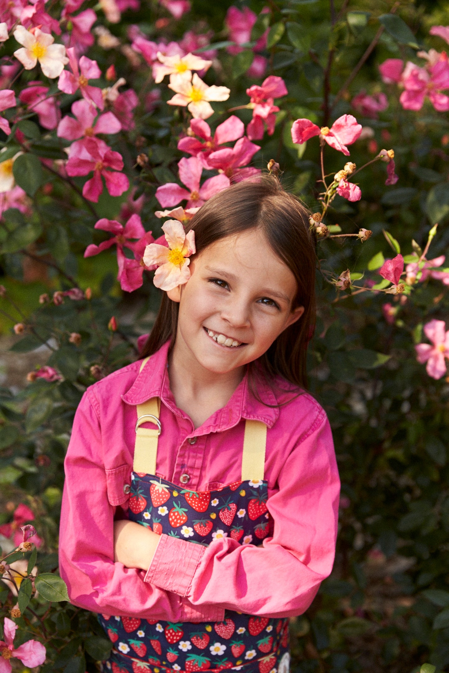 Young girl in a pink shirt and colorful overalls standing among flowers