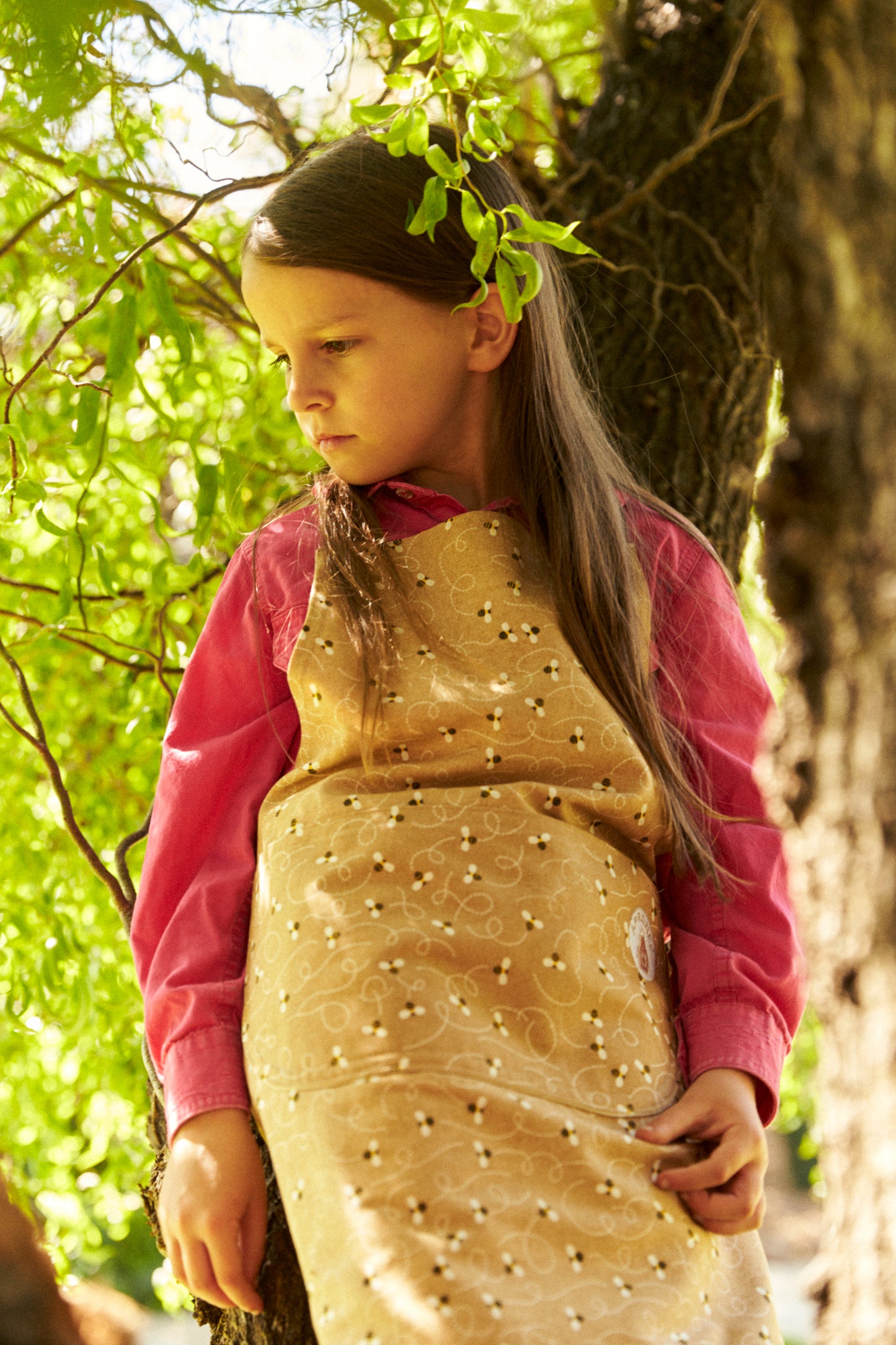 Young girl in a gold dress with pink sleeves standing under a tree