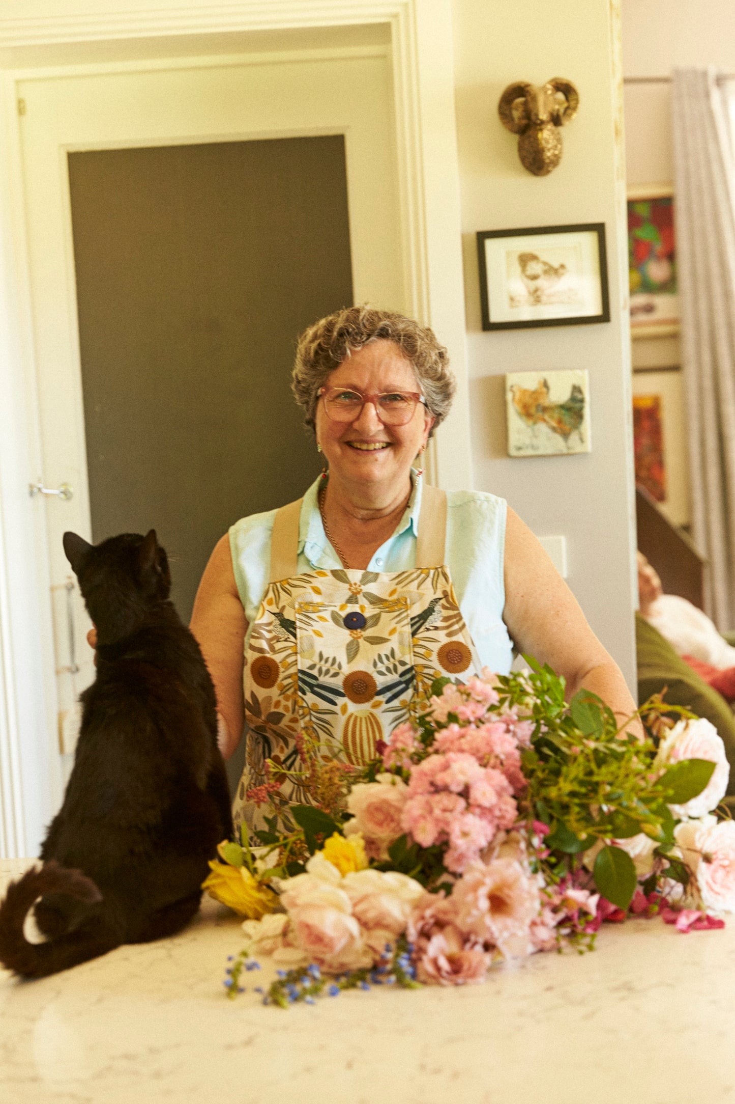Woman in a kitchen with flowers and a black cat
