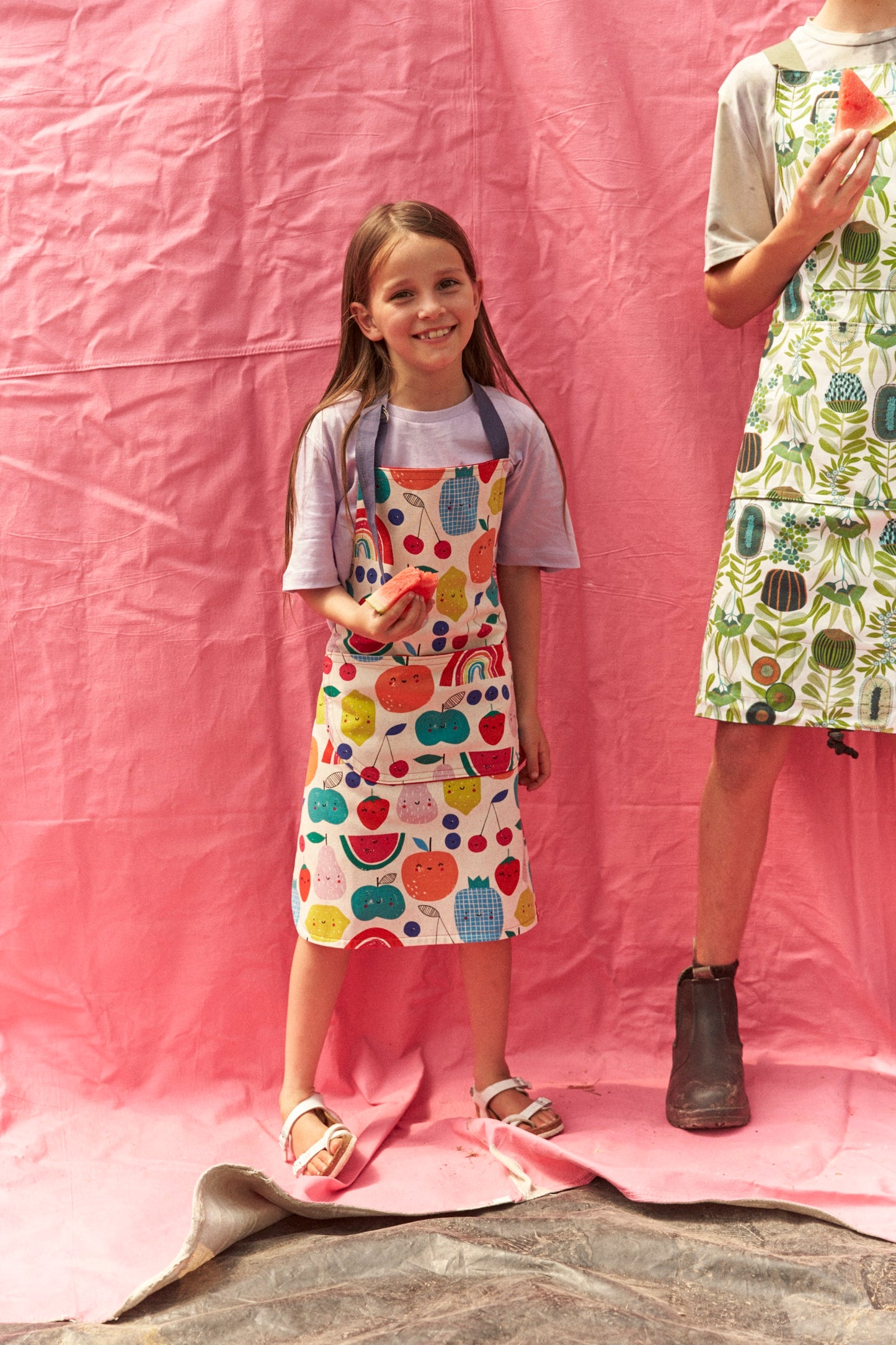 Child wearing a colorful apron with fruit patterns on a pink background