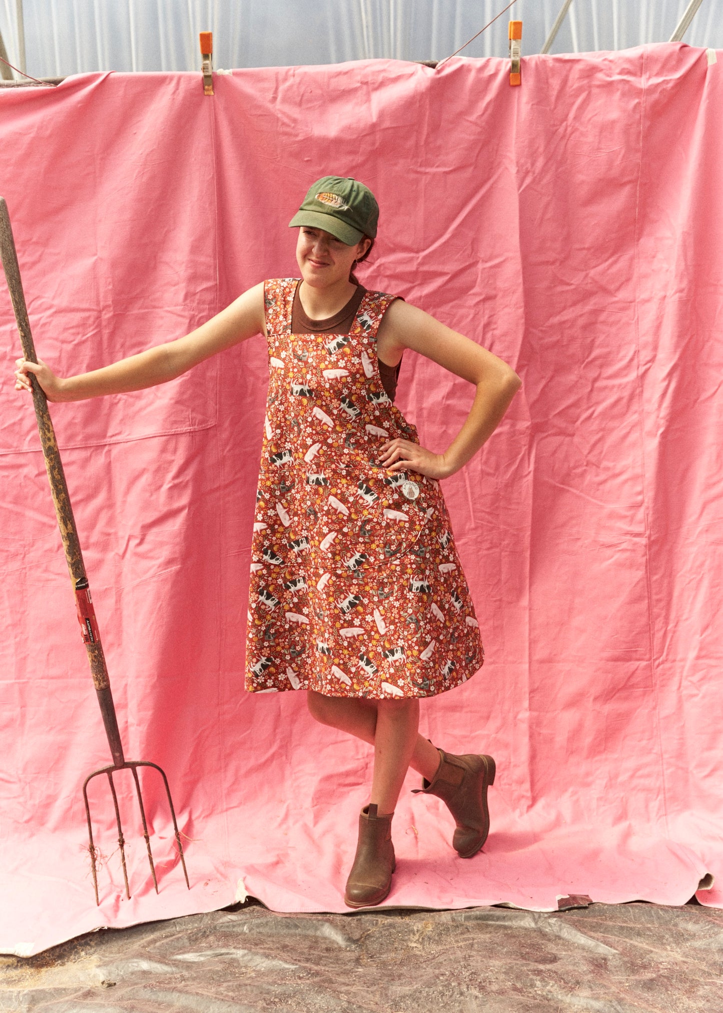 Person in a floral dress standing next to a pink backdrop with a garden fork.