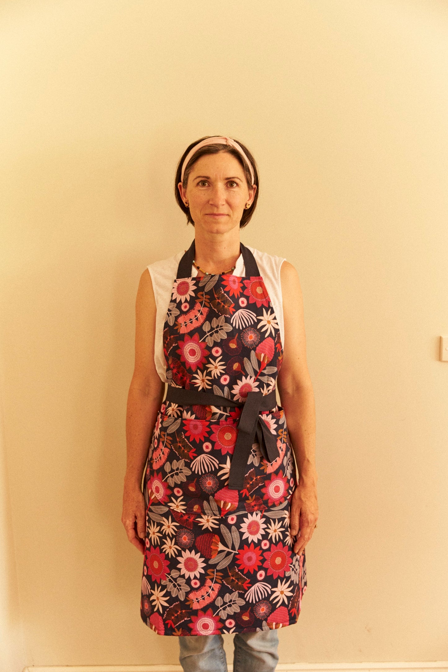 Person wearing a floral apron against a plain wall