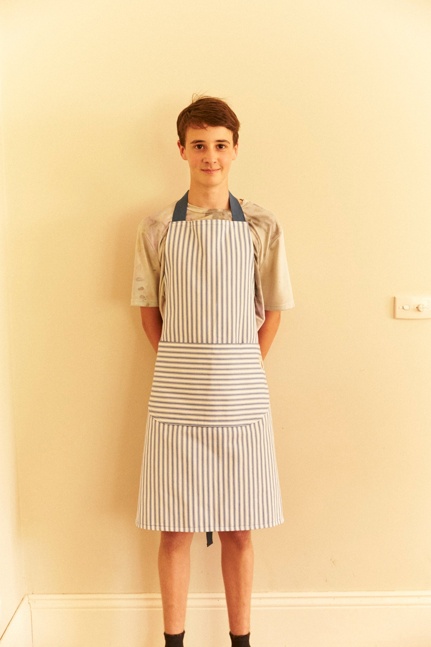 Person wearing a striped apron against a plain wall