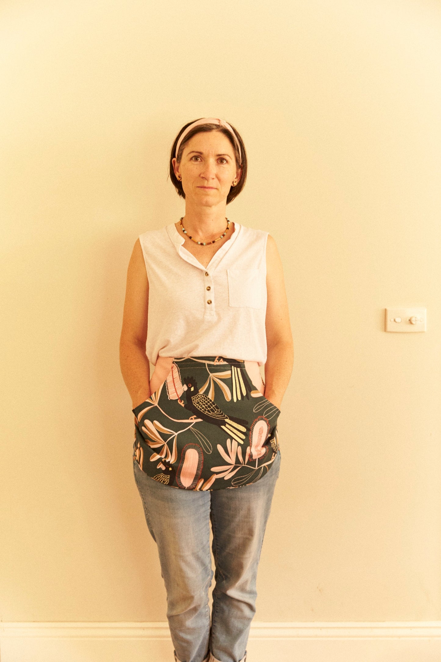 Woman wearing a white sleeveless shirt and patterned pants against a beige wall.