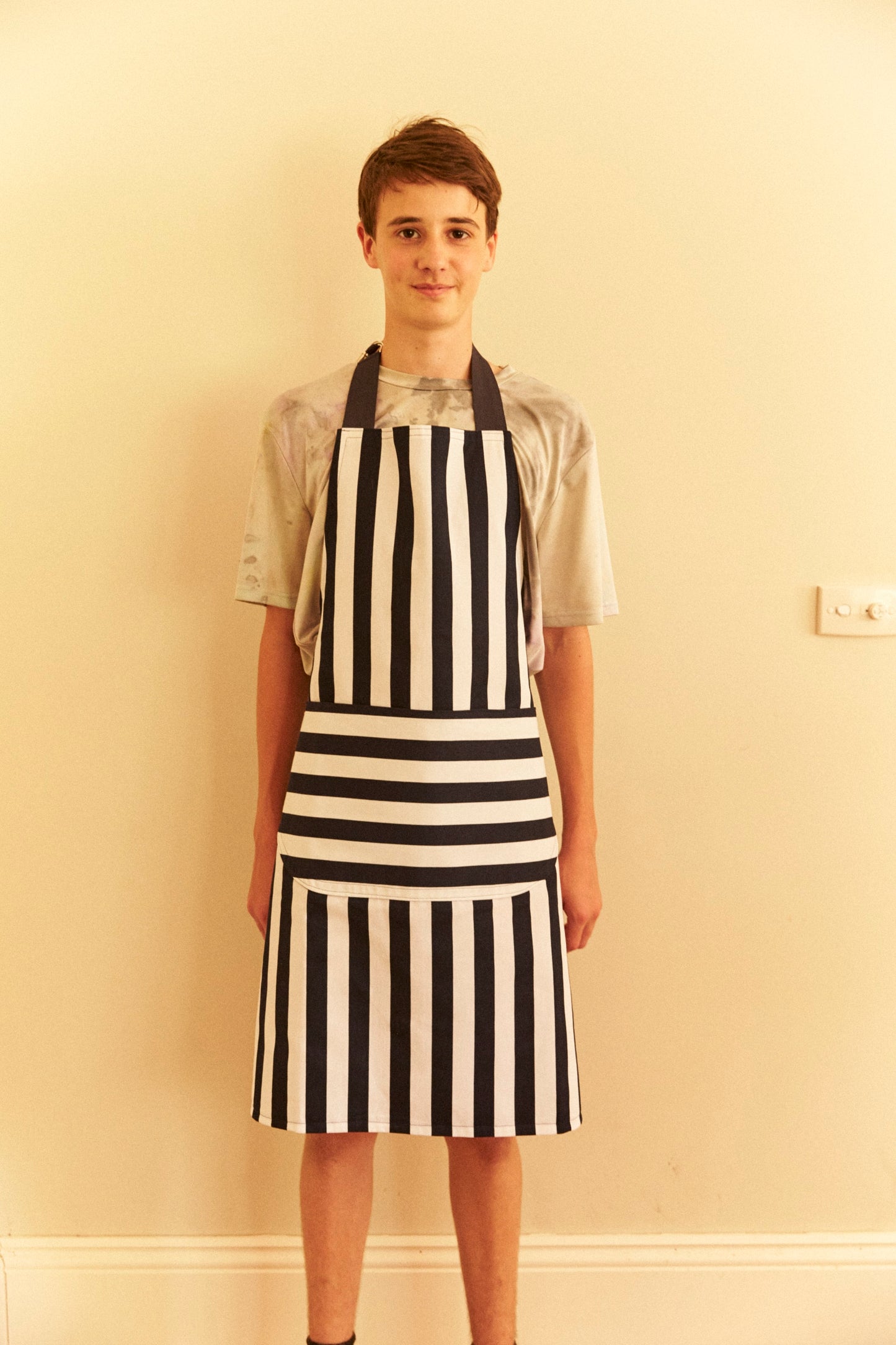 Person wearing a black and white striped apron against a beige wall.