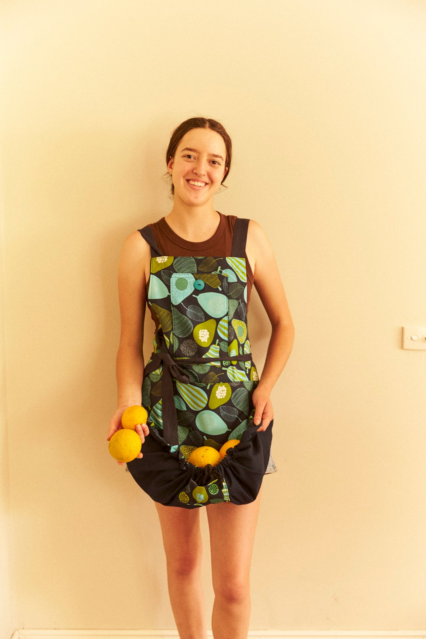 Woman wearing a sleeveless dress with a leaf pattern against a plain wall.
