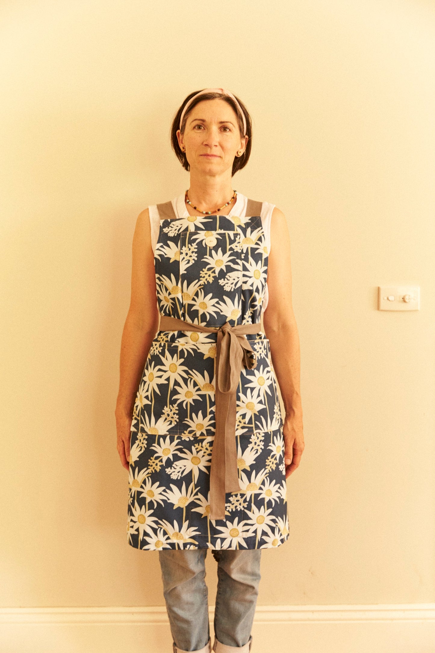Person wearing a floral apron against a plain wall
