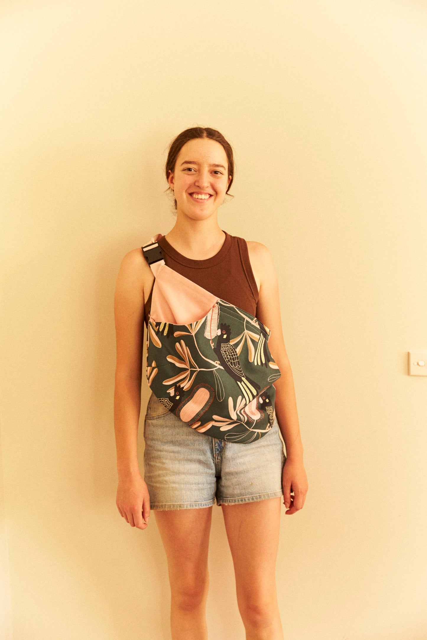 Person wearing a sleeveless top with a floral design and denim shorts against a beige wall.