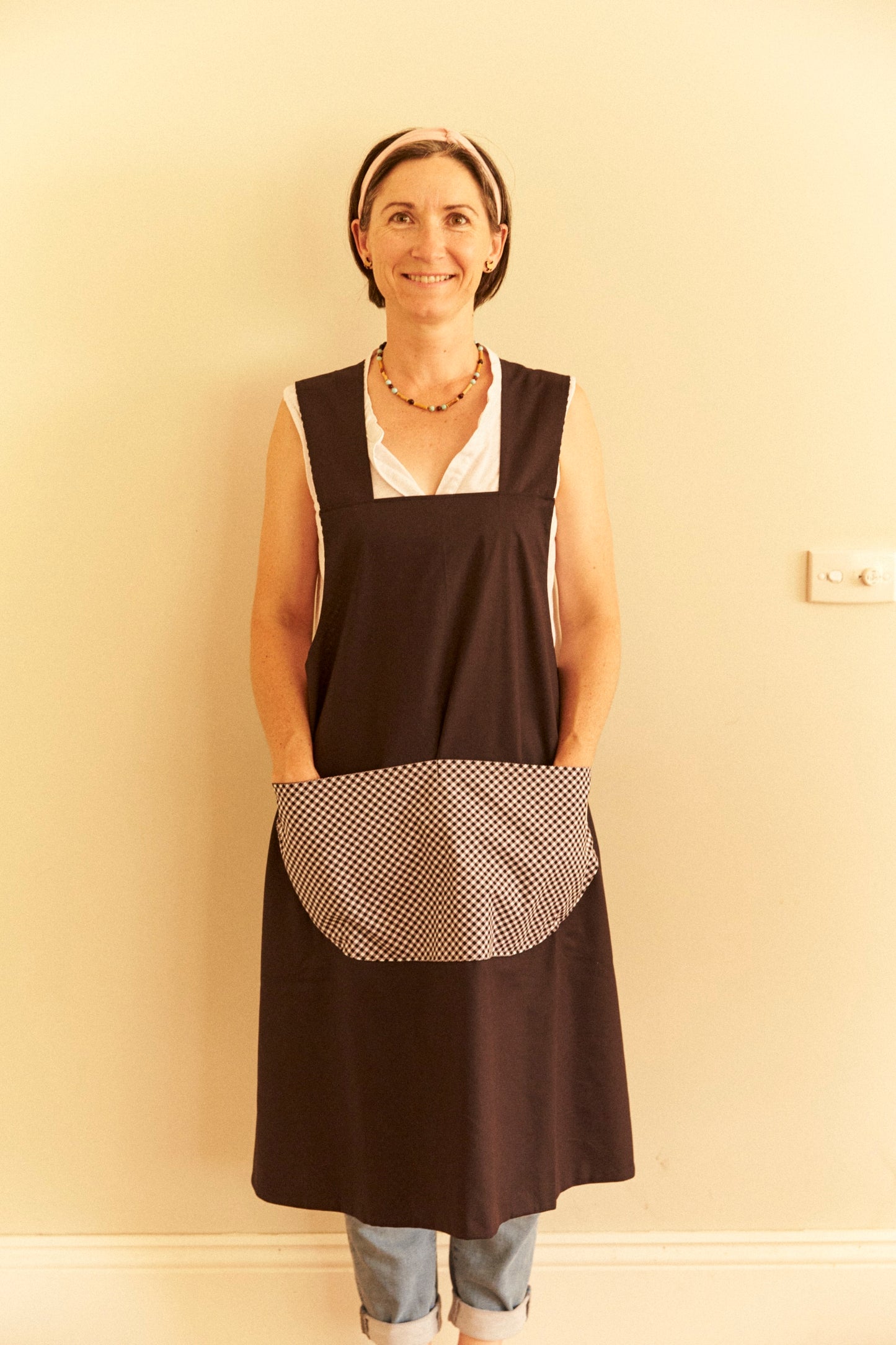 Woman wearing a black apron with a white pocket against a beige wall.