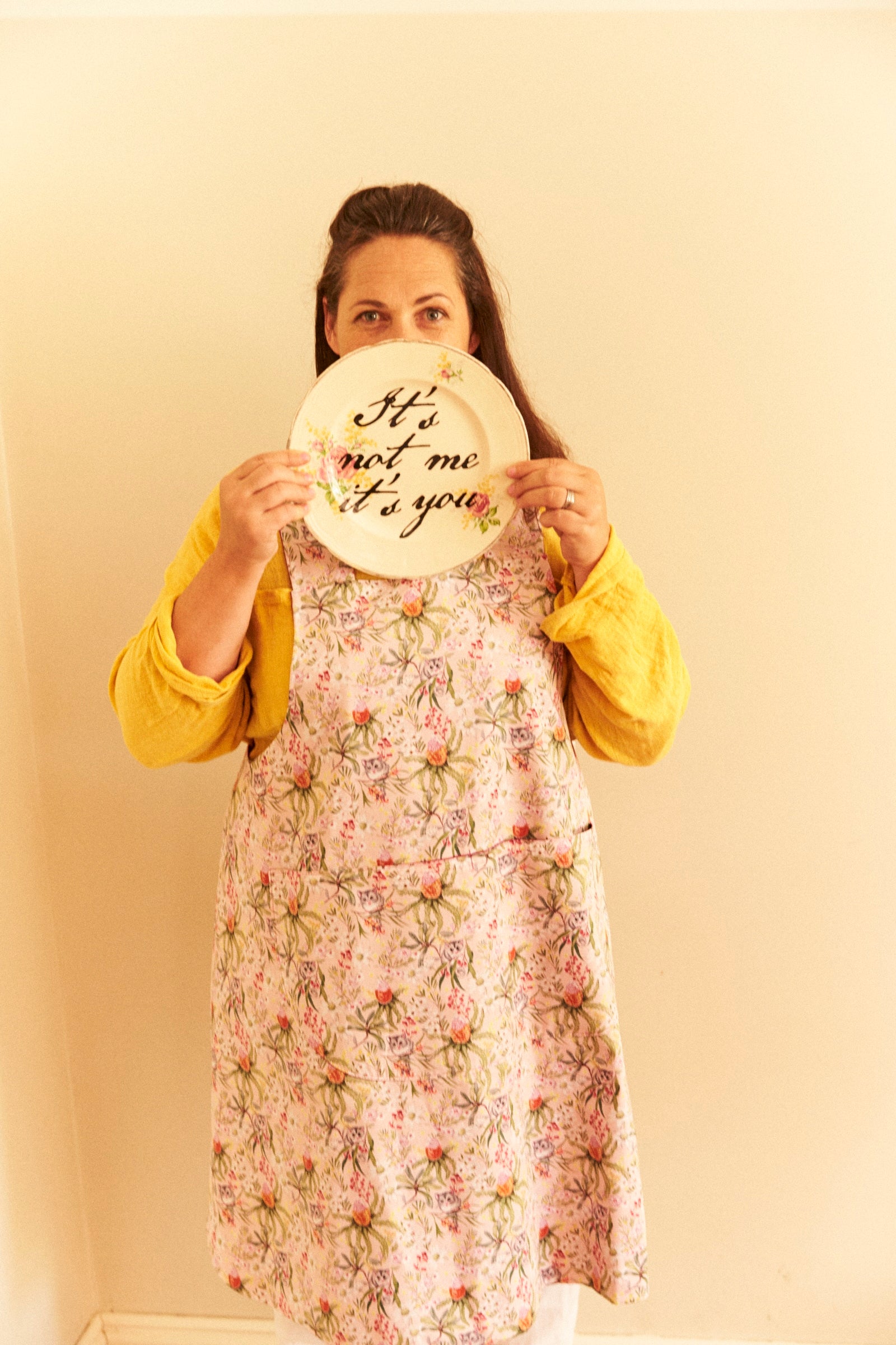 Person wearing a floral dress holding a plate with text against a plain background