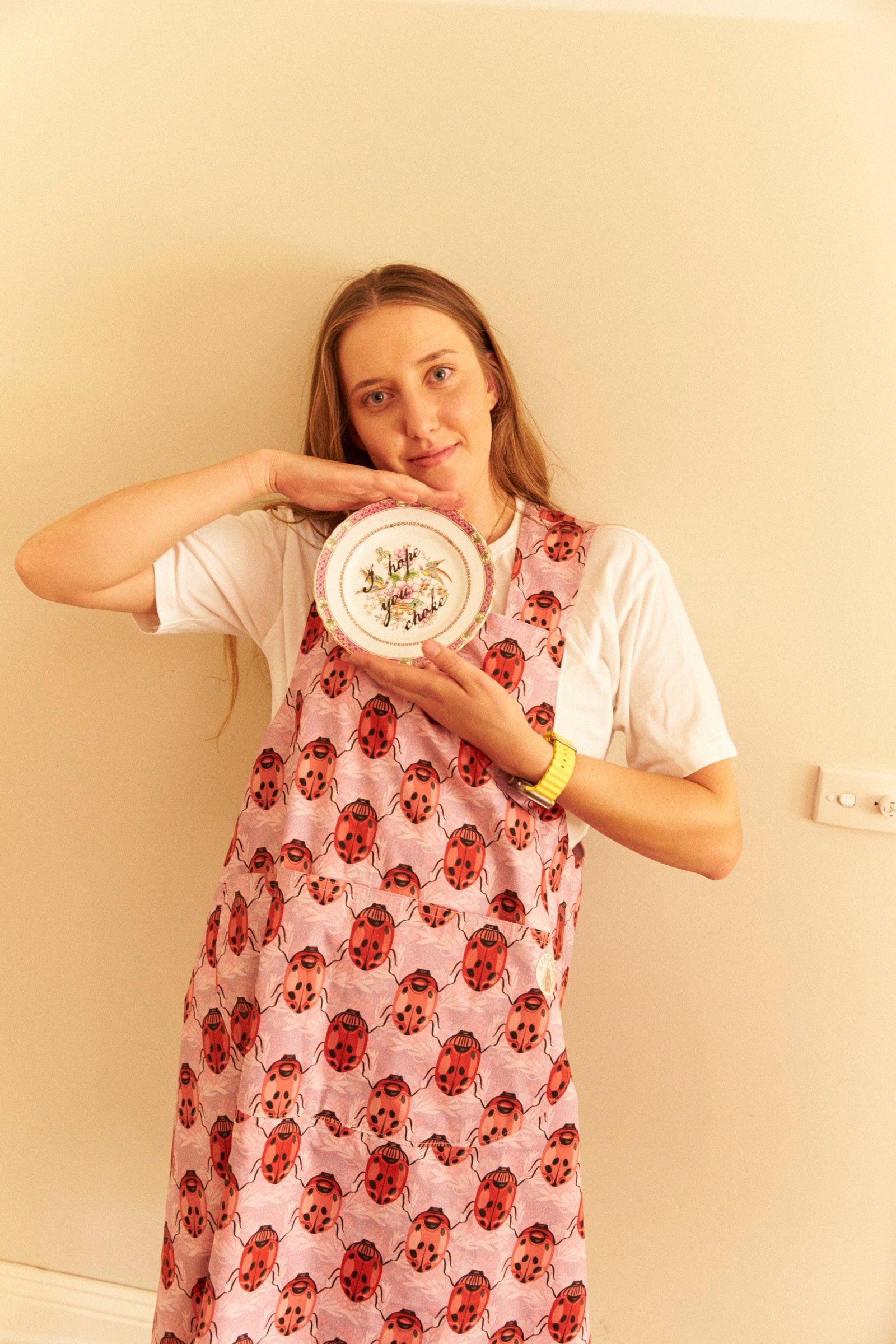 Woman wearing a floral dress holding a plate with a decorative design against a plain wall.