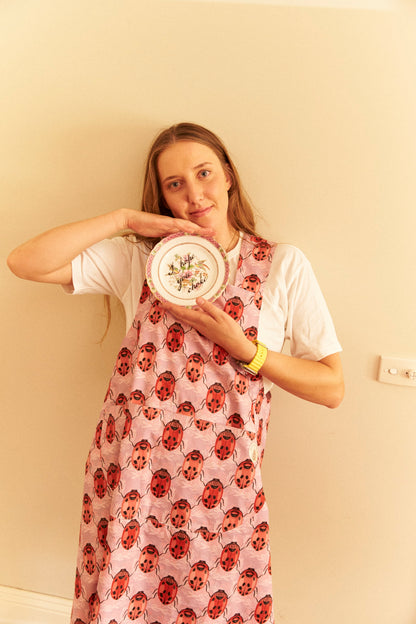 Woman wearing a floral dress holding a plate with a decorative design against a plain wall.