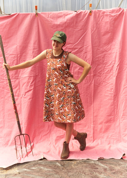 Person in a floral dress standing next to a pink backdrop with a garden fork.