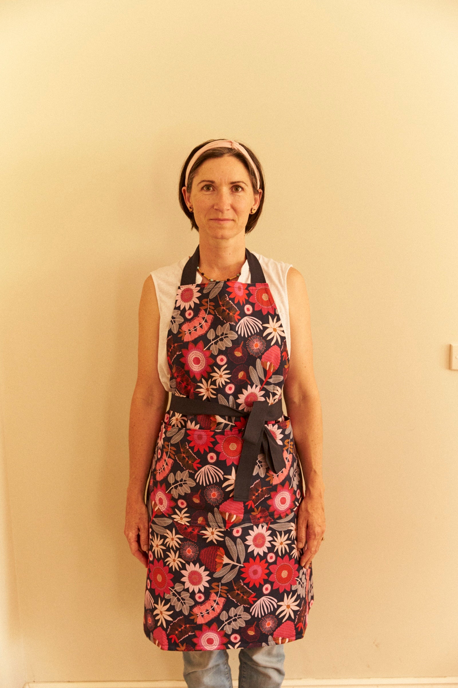 Person wearing a floral apron against a plain wall