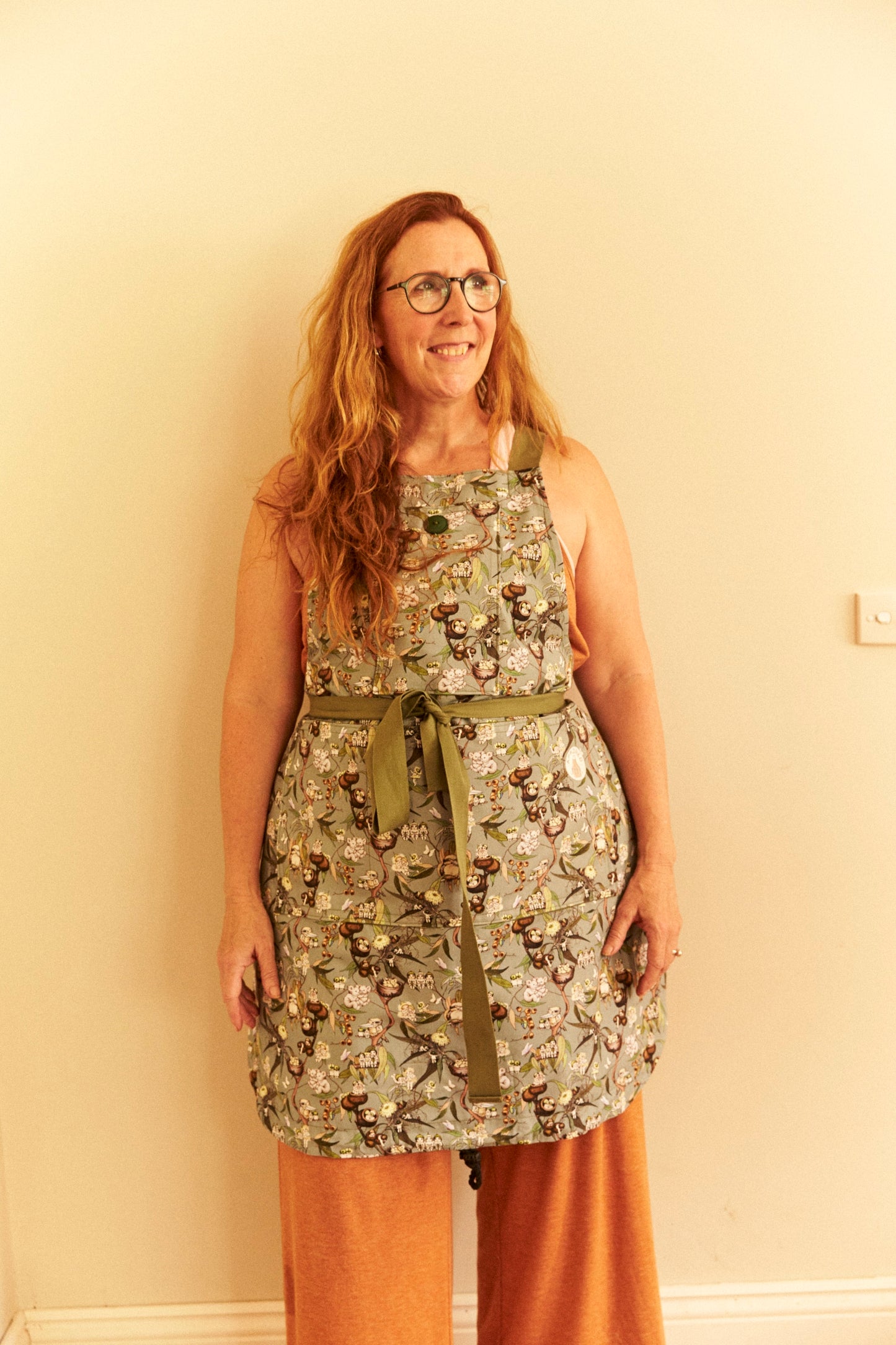 Woman wearing a floral apron standing against a plain wall.