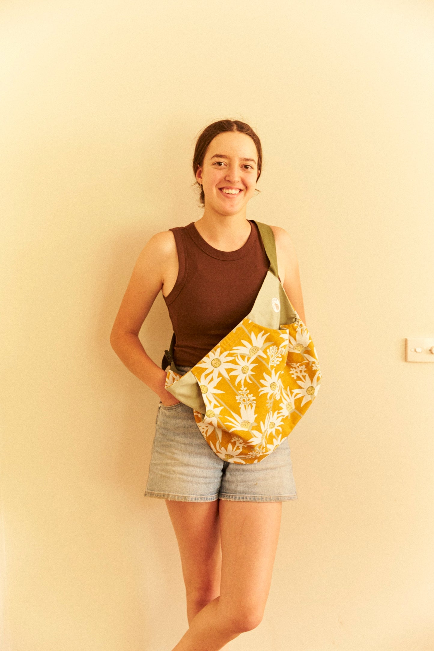 Woman holding a yellow floral bag against a beige wall