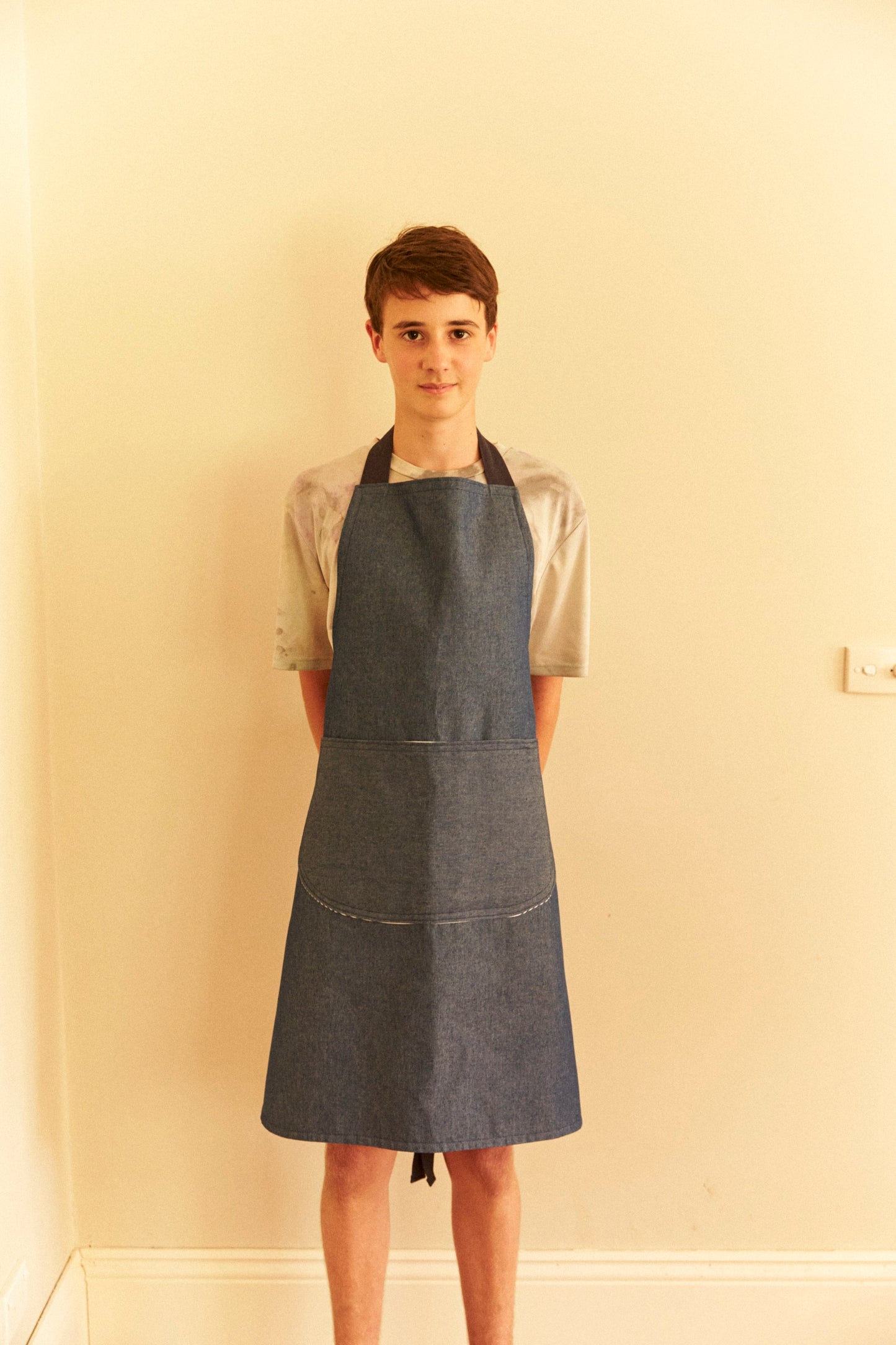 Person wearing a denim apron against a plain wall