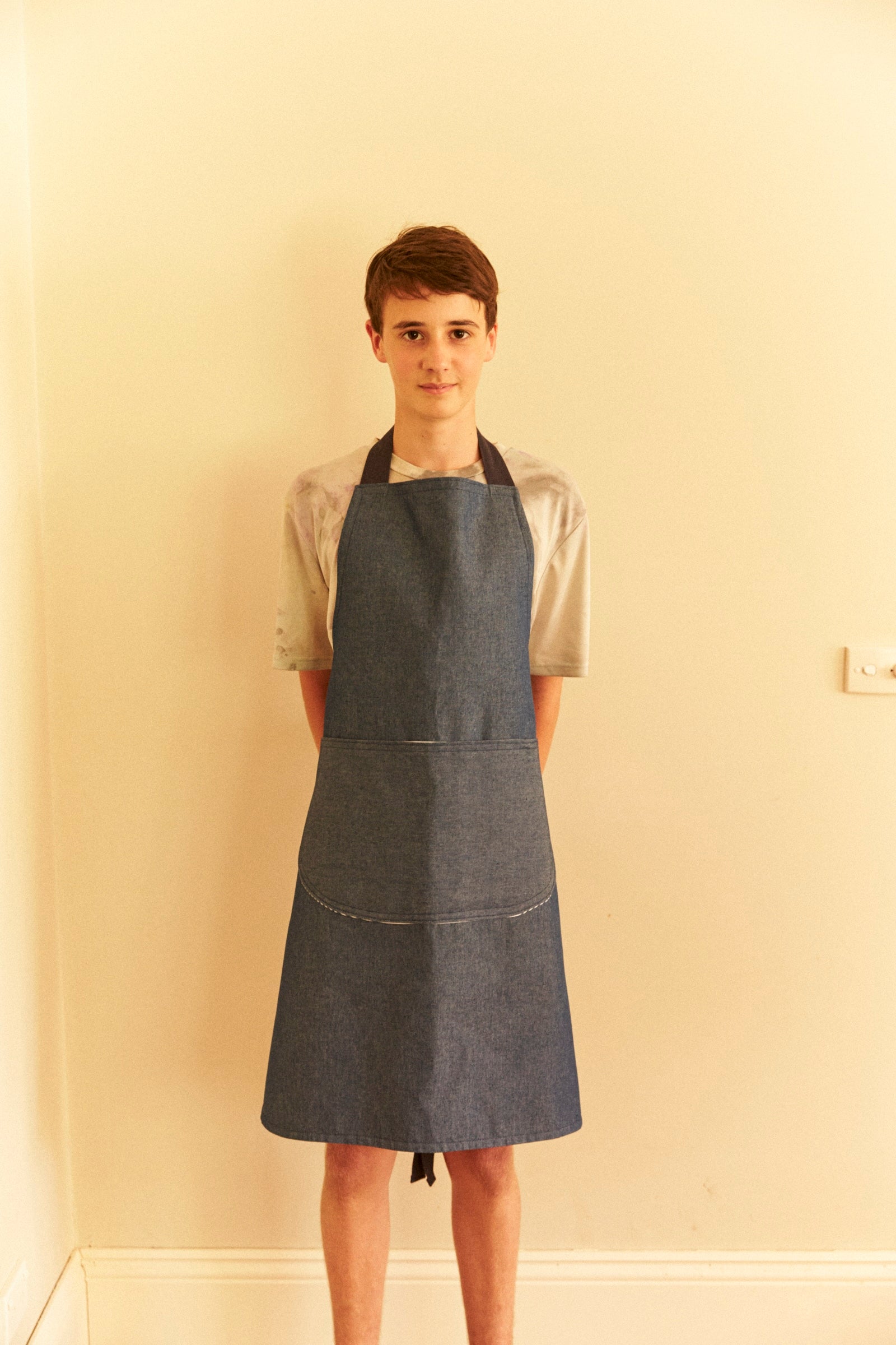 Person wearing a denim apron against a plain wall