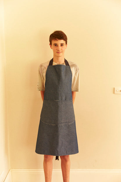 Person wearing a denim apron against a plain wall