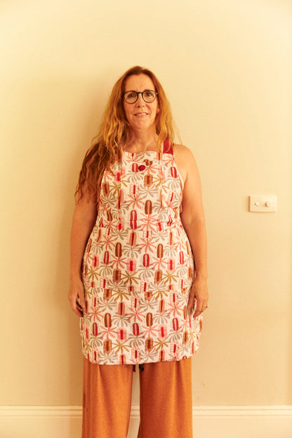 Woman wearing a patterned apron standing against a plain wall.