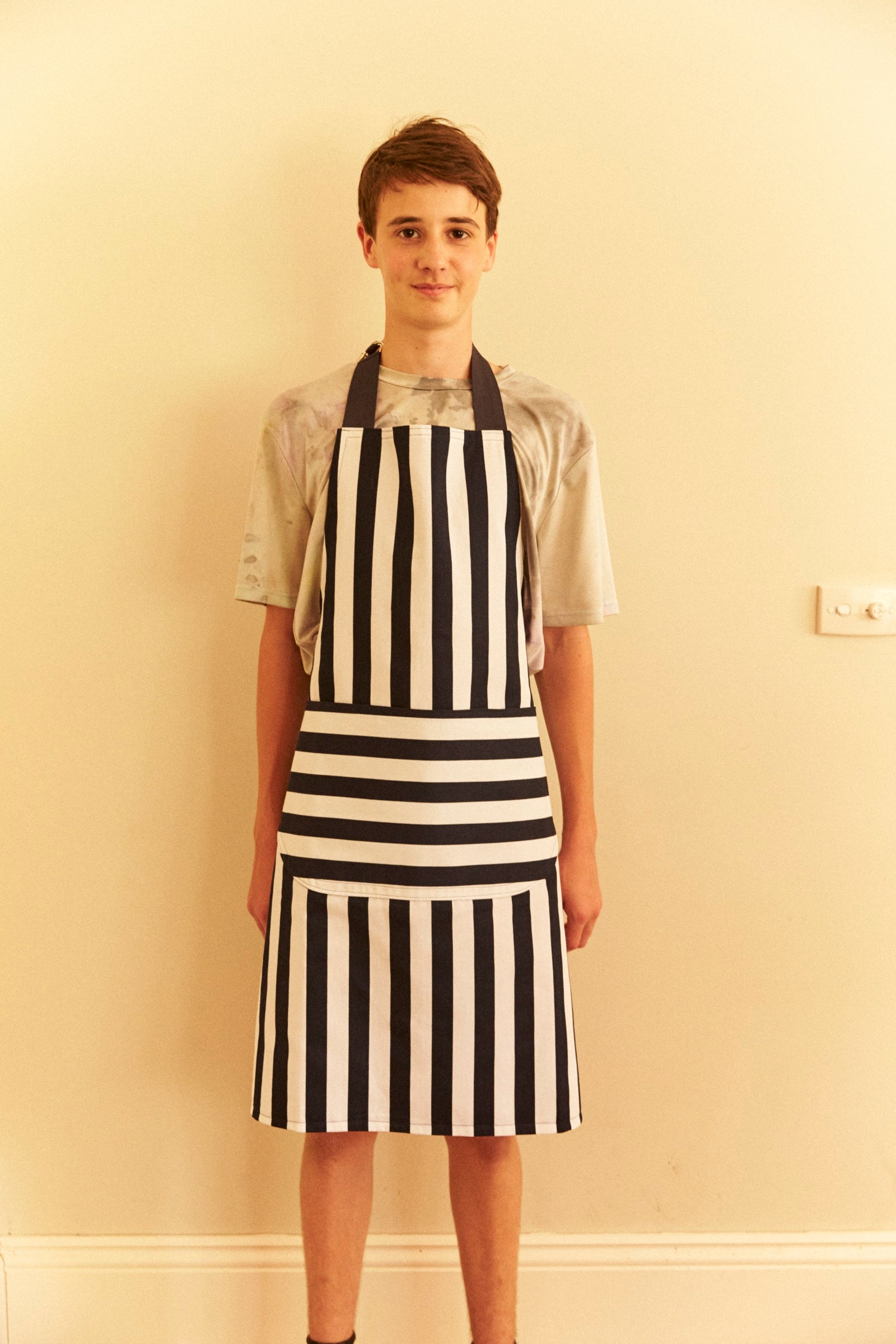 Person wearing a black and white striped apron against a beige wall.