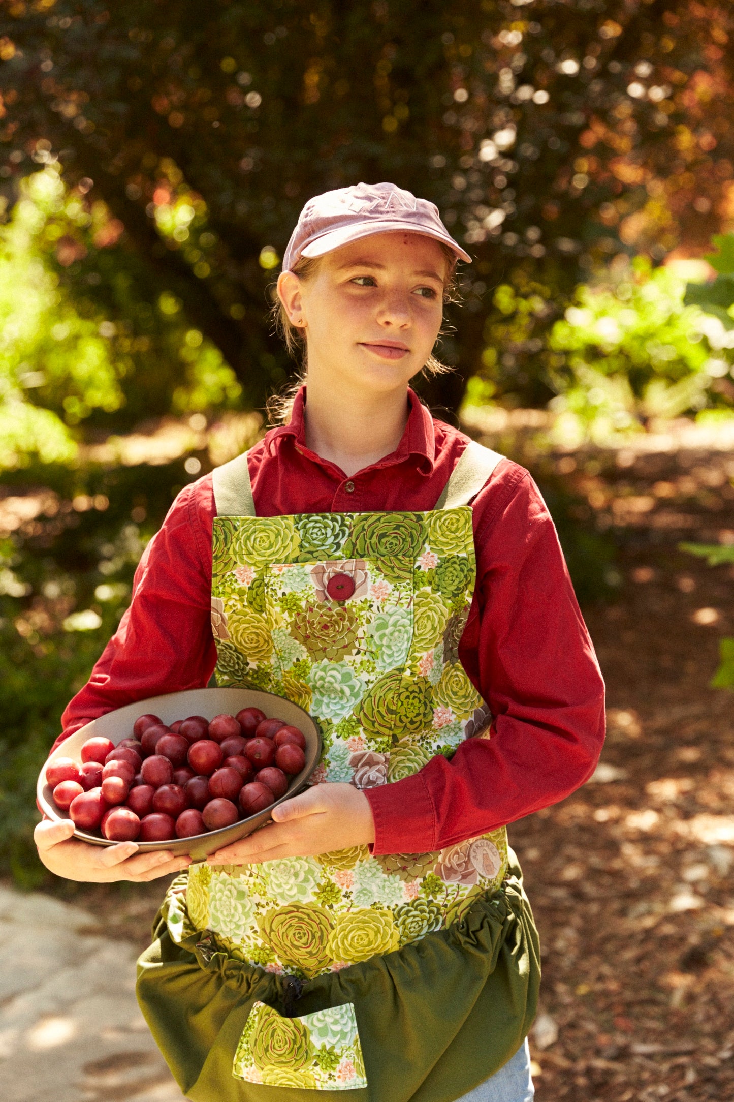Person holding a bowl of fruits in a garden setting