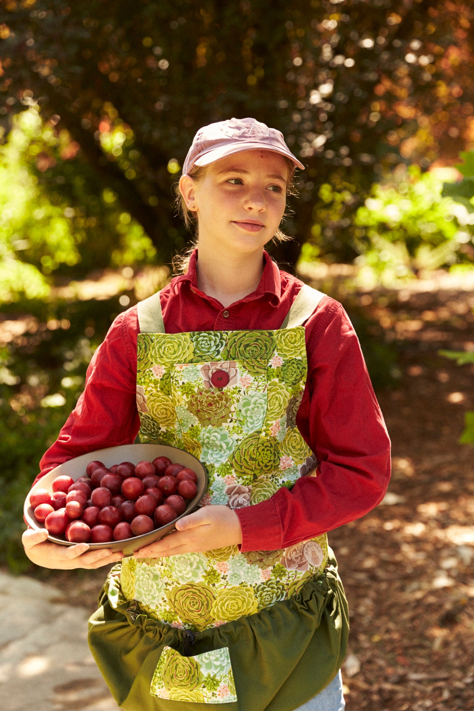 Person holding a bowl of fruits in a garden setting