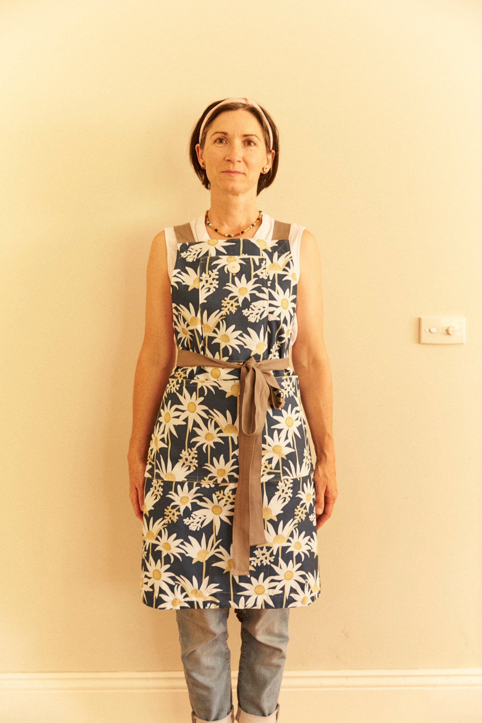 Person wearing a floral apron against a plain wall