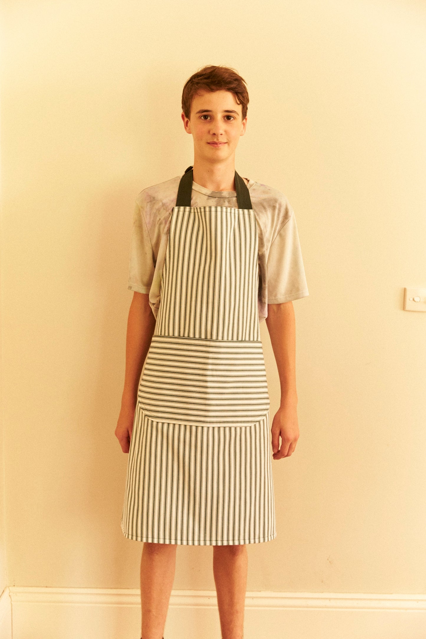 Person wearing a striped apron against a plain wall