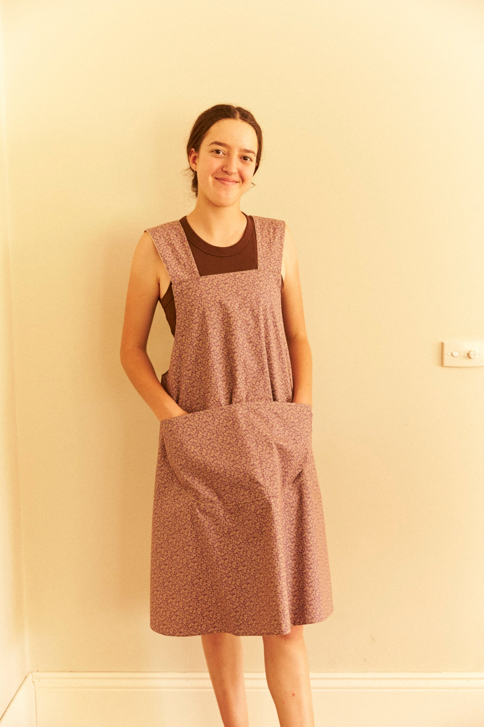 Woman wearing a brown patterned dress against a beige wall.